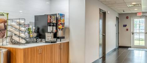 Una recepción limpia y moderna con una máquina de café, dispensador de zumo y una barra con estación de café.