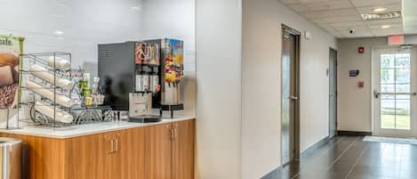 A clean, modern reception area with a coffee machine, a juice dispenser, and a display of coffee cups.