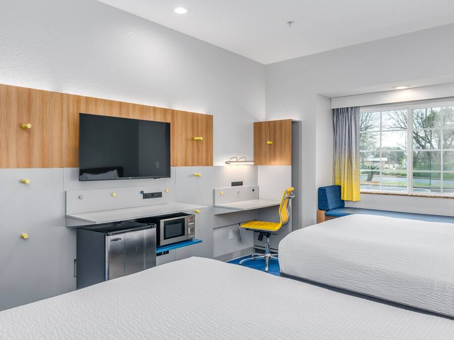 Ein Hotelzimmer mit Bett, Schreibtisch mit Computer, Fernseher und einem Fenster mit Vorhängen.