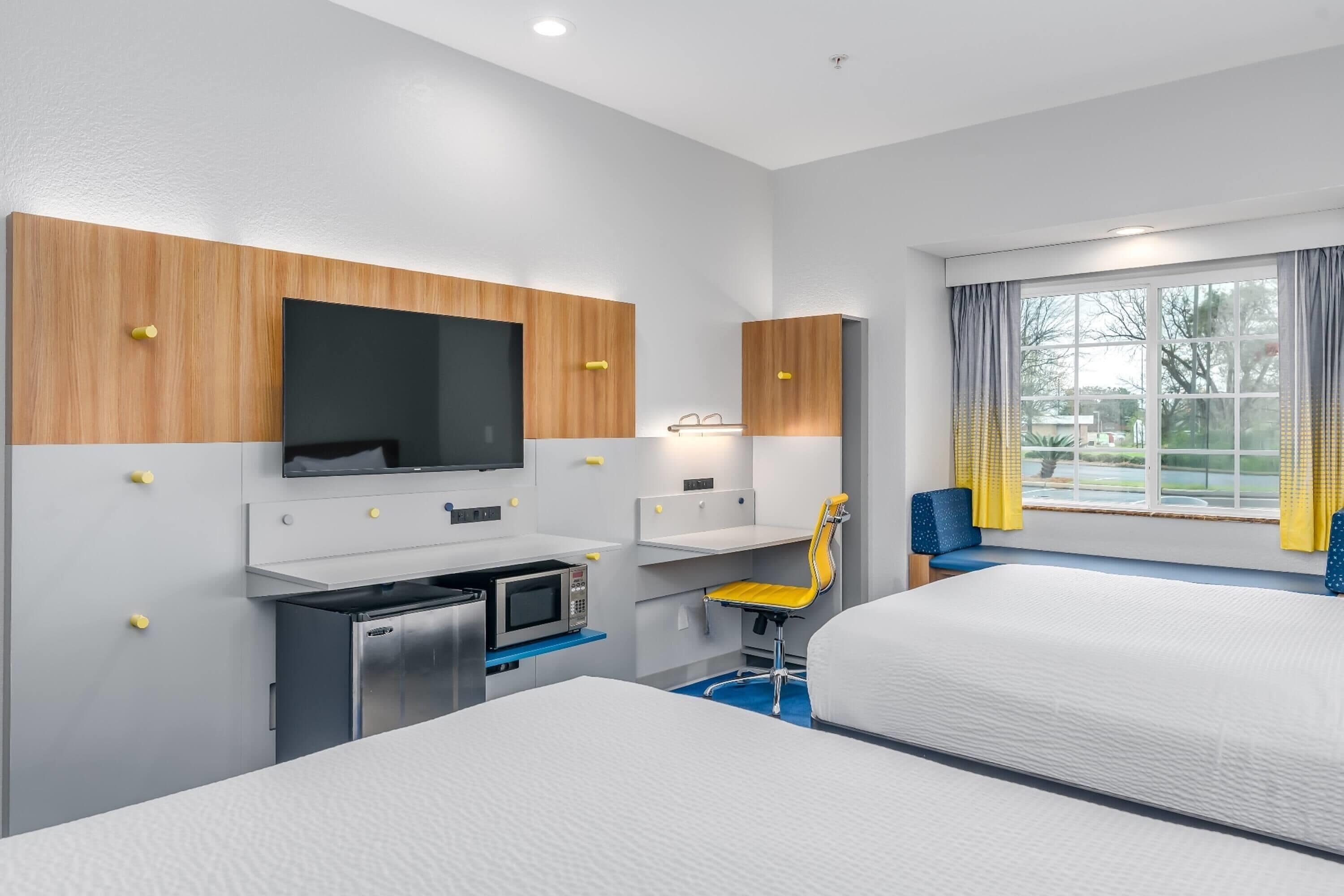 Habitación de hotel con dos camas, un escritorio con microondas, televisor y una silla.
