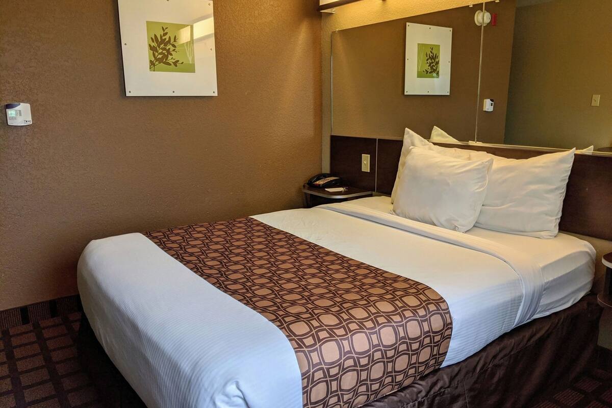 A hotel room with a bed, a nightstand, a telephone, and two framed pictures on the wall.
