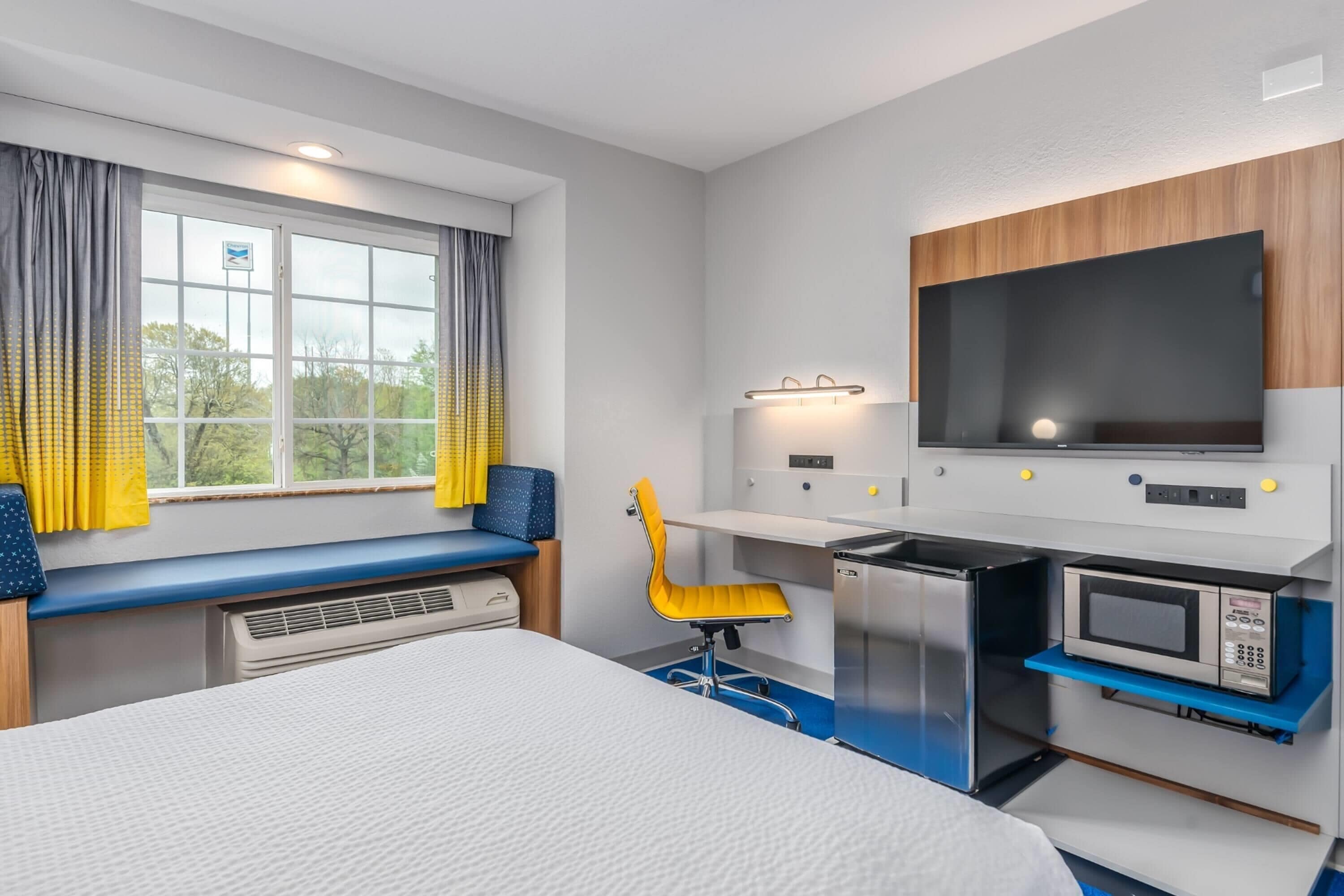 Habitació d'hotel amb un llit, una taula de treball amb un ordinador, un microones i una televisió.