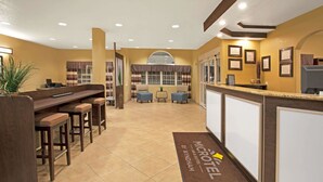 A hotel lobby with a reception desk, bar area with stools, seating area with chairs, and a large window with curtains. - Microtel Inn & Suites by Wyndham Cartersville (Cartersville)