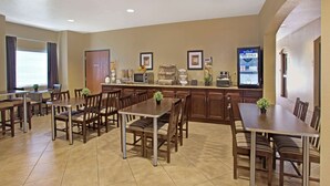 A hotel dining area with multiple tables and chairs, a kitchen counter, and a beverage dispenser. - Microtel Inn & Suites by Wyndham Cartersville (Cartersville)