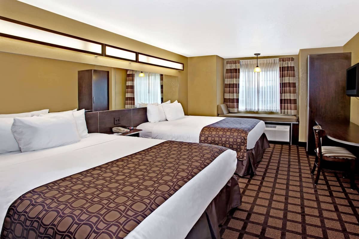 A hotel room with two beds, a desk, a chair, and a television.