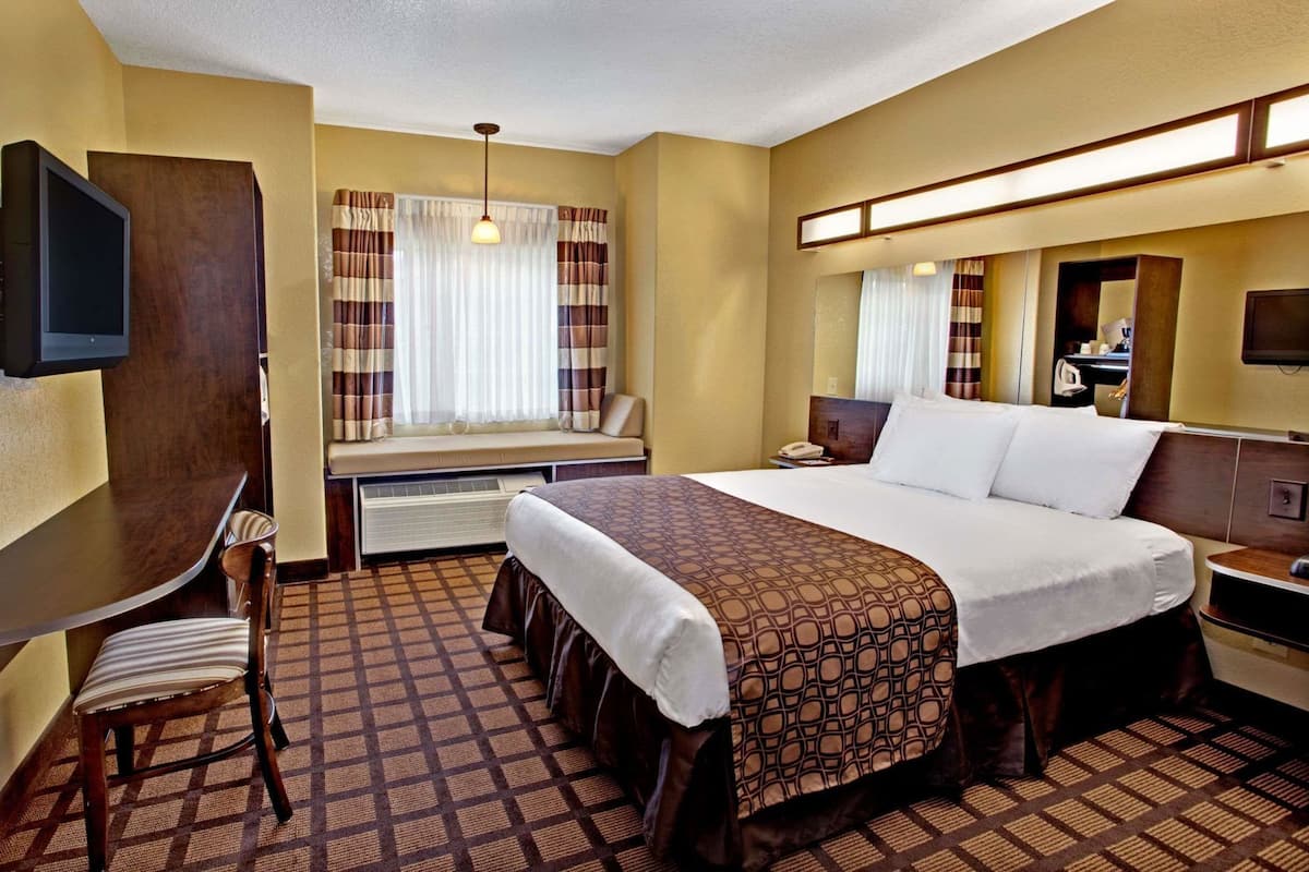 A hotel room with a bed, a desk, a chair, a television, and a window with curtains.