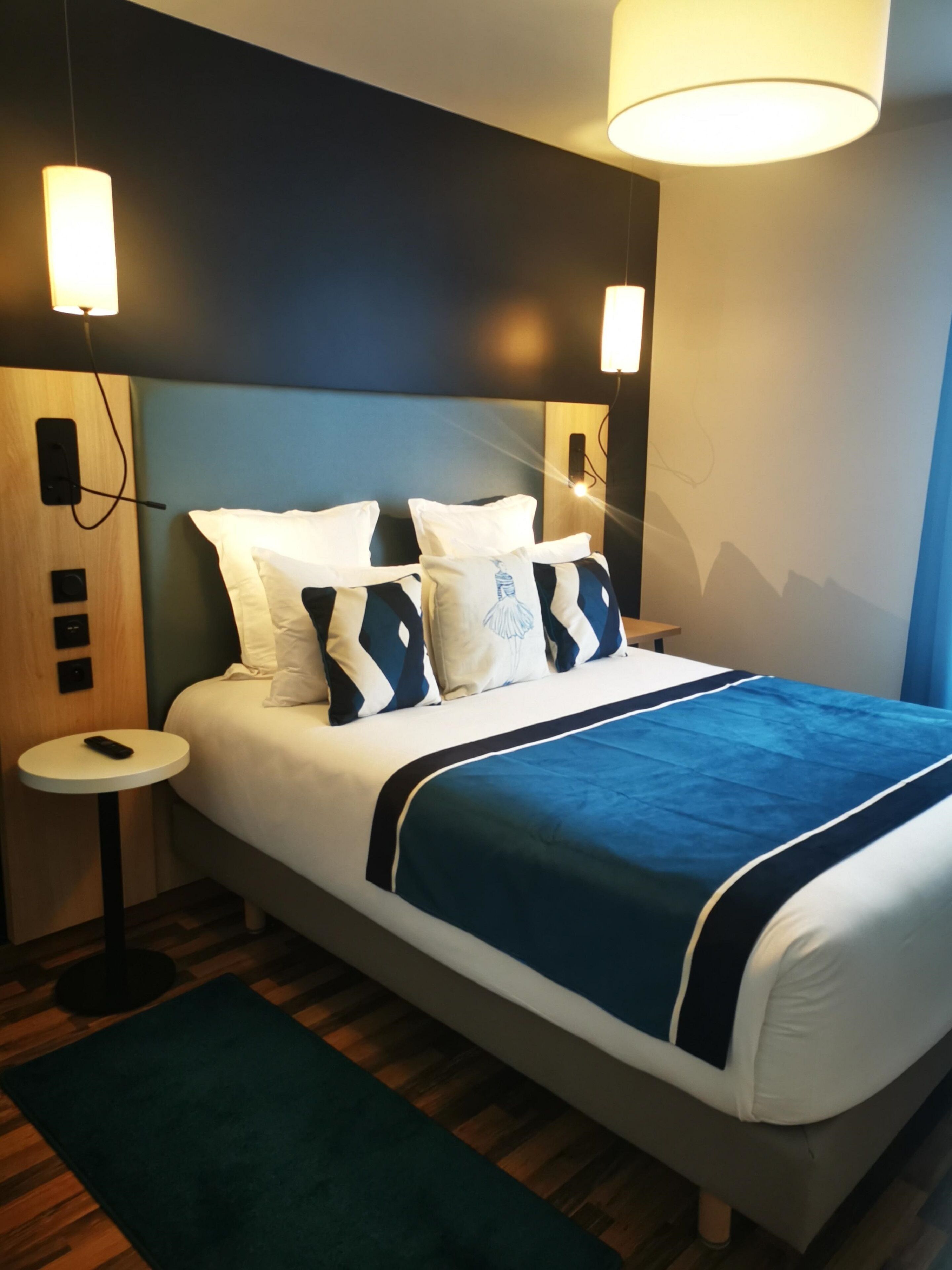 Une chambre d’hôtel moderne avec un grand lit, deux tables de chevet et une petite table d’appoint.