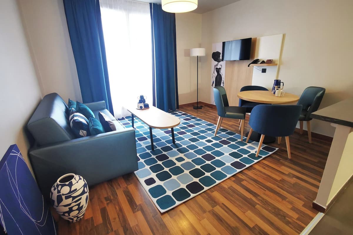 Een moderne woonkamer met een bank, een salontafel, een eettafel met stoelen, een vloerkleed met patroon en een flatscreen televisie die aan de muur is bevestigd.