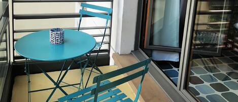 A balcony with a blue table and chairs, a white wall, and a glass door.