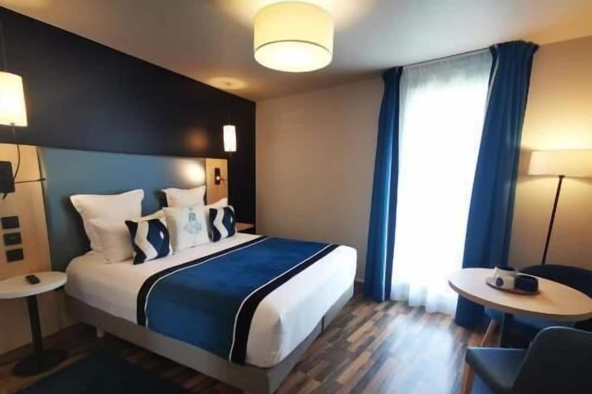 Een hotelkamer met een bed, nachtkastjes, een bureau, een stoel en een raam met gordijnen.