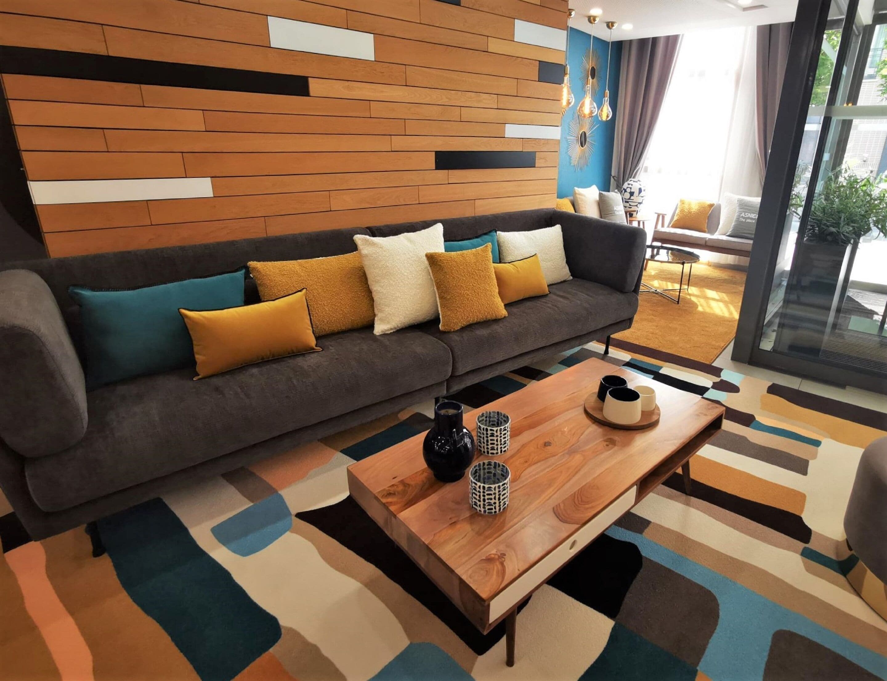 Un salon moderne avec un canapé gris, des coussins colorés, une table basse en bois et un tapis à motifs.