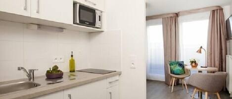 A modern kitchen with white cabinets, a microwave, and a sink. There is a dining area with a table, chairs, and a TV.