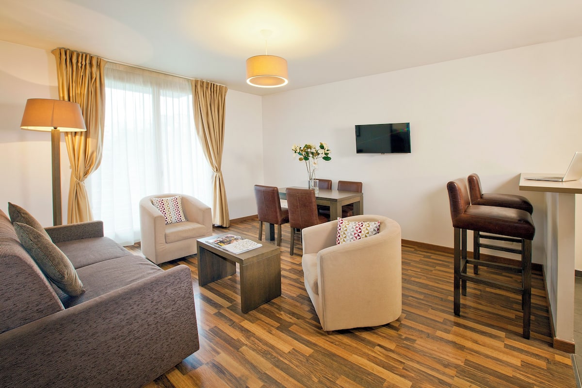 Una sala de estar moderna con un sofá, sillones, una mesa de centro y un comedor con sillas y una mesa.