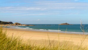 A beach with clear skies, calm waters, and a distant island with a lighthouse. - Résidence Lagrange Vacances Cap Green (Frehel)