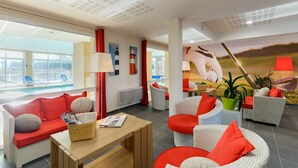 A modern hotel room with a pool view, wicker furniture, and red accents. - Résidence Lagrange Vacances Cap Green (Frehel)