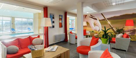 Habitación de hotel moderna con vista a la piscina, mobiliario de mimbre y detalles en rojo.