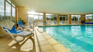 An indoor swimming pool with clear blue water, surrounded by sunlit windows and blue lounge chairs. - Résidence Lagrange Vacances Cap Green (Frehel)