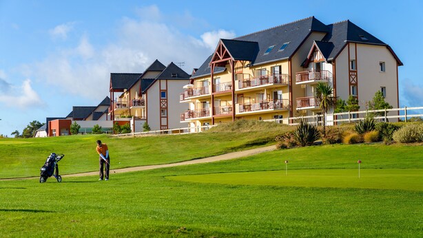 A golf course with a clubhouse and a building with multiple balconies. - Résidence Lagrange Vacances Cap Green (Frehel)