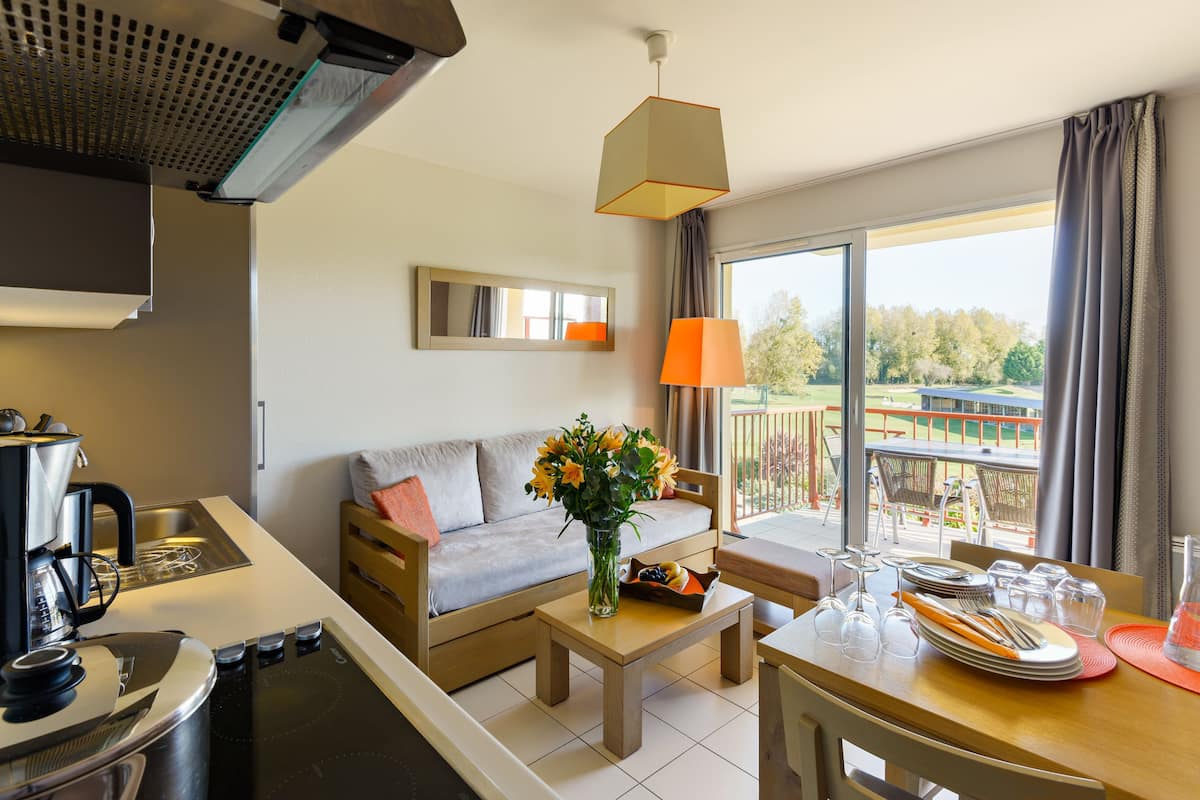 A modern kitchen with a coffee maker, a dining area with a table set for two, a sofa, and a balcony with a view of a golf course.