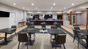 A spacious indoor area with multiple tables and chairs, a reception desk, and a counter with various items. - Baymont by Wyndham Texas City (Texas City)