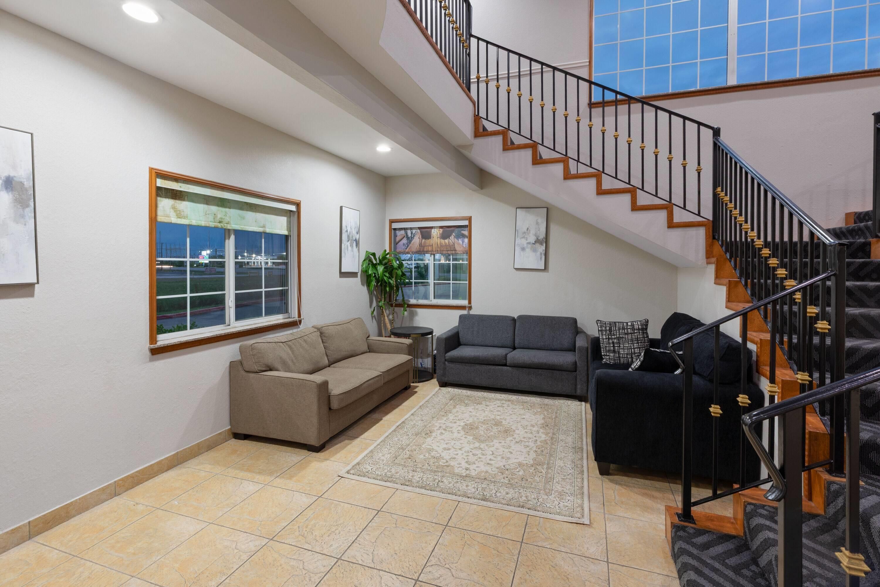 A spacious living area with a high ceiling, a staircase with wooden steps and black railings, and a large window offering a view of the outdoors.