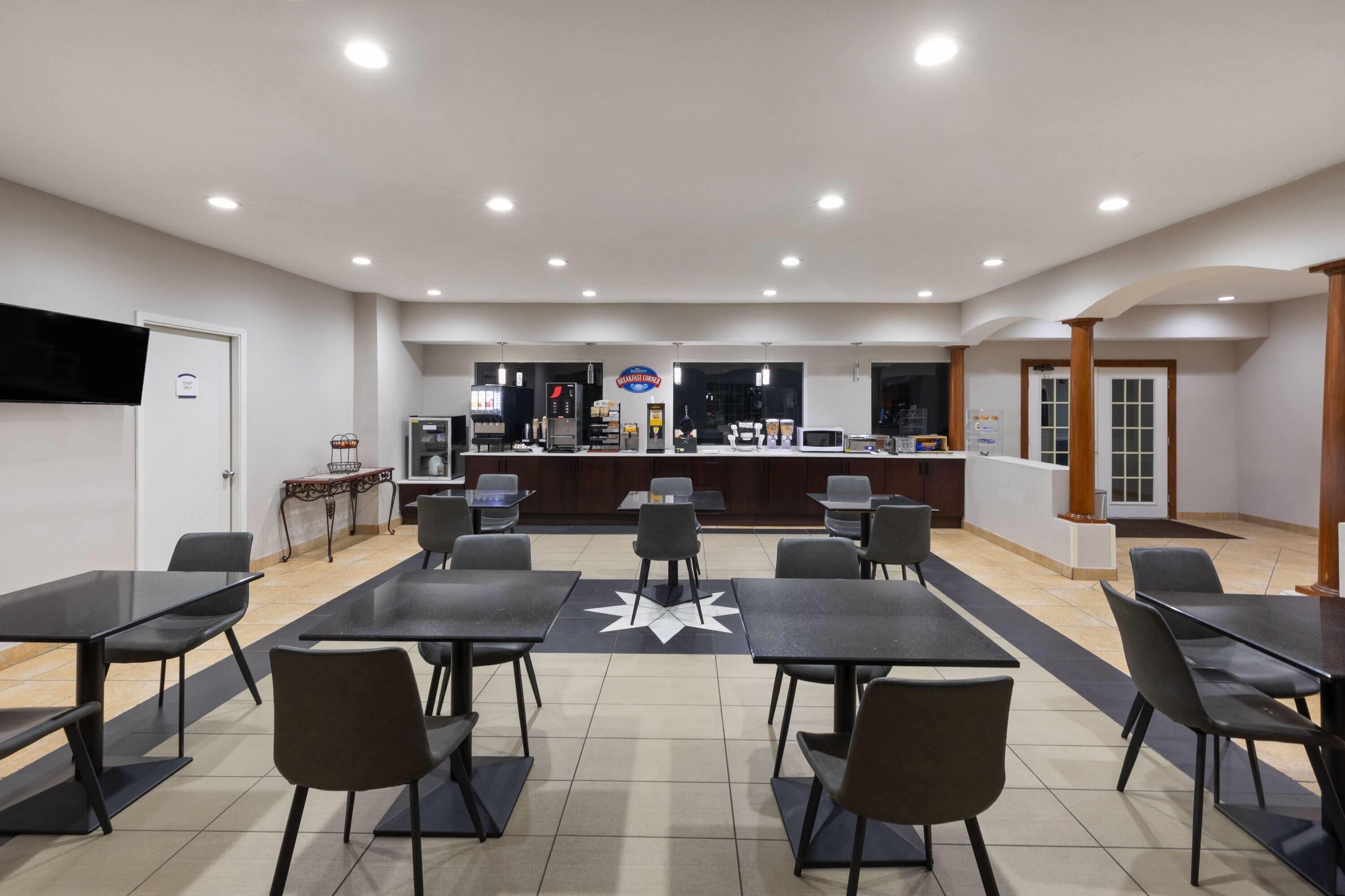 A spacious indoor area with multiple tables and chairs, a counter with a sign, and a television on the wall.