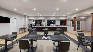 A spacious indoor area with multiple tables and chairs, a counter with a sign, and a television on the wall.