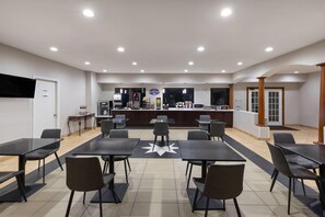 A spacious indoor area with multiple tables and chairs, a counter with a sign, and a television on the wall. - Baymont by Wyndham Texas City (Texas City)