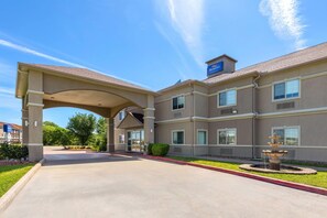 A hotel entrance with a covered walkway, a fountain, and a clear blue sky.