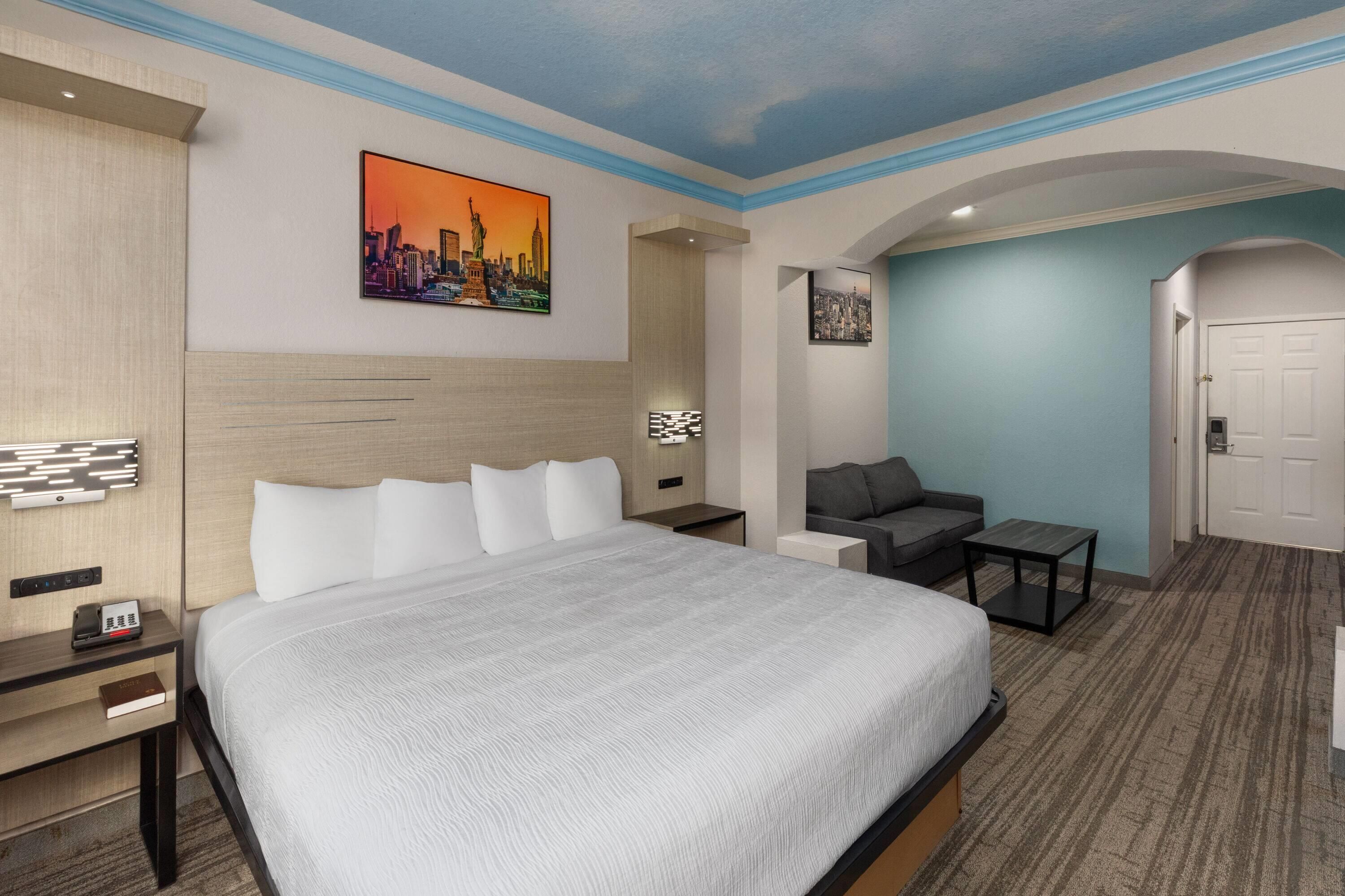Una habitación de hotel con una cama, un área de descanso con un sofá y una mesa, y una puerta que da a otra habitación.