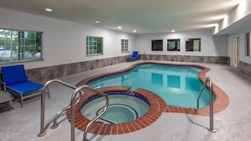 An indoor swimming pool with a tiled edge, a blue lounge chair, and a window with a view of trees.