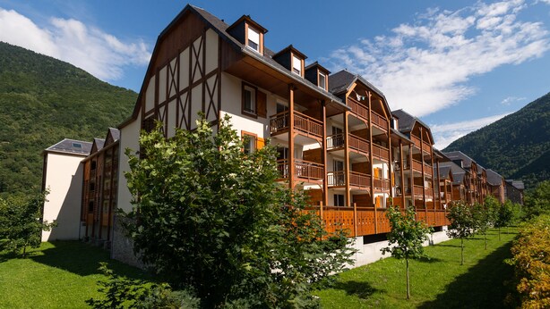 A multi-story chalet with a traditional Alpine architectural style, featuring wooden balconies and a lush garden. - Résidence Lagrange Vacances le Belvédère (Saint-Mamet)