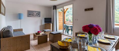 Una sala de estar moderna con un sofá, un televisor y un comedor con una mesa lista para dos.