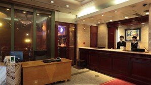 A hotel reception area with a wooden reception desk, a computer, and a bar visible through the glass doors. - Hotel Arca Torre Roppongi (Tokyo)