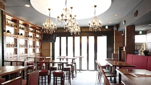 A restaurant interior with wooden tables and chairs, a bar area with shelves of bottles, and a large window with natural light. - Hotel Arca Torre Roppongi (Tokyo)