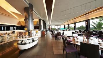 Un espace de restauration moderne doté d’un îlot central, de longues tables et d’un plafond haut avec un éclairage linéaire.