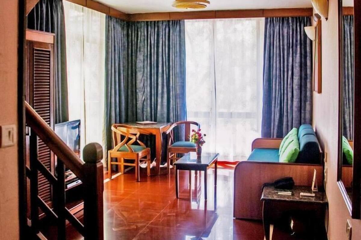 A room with a staircase, a dining area, a sofa, and a window with curtains.