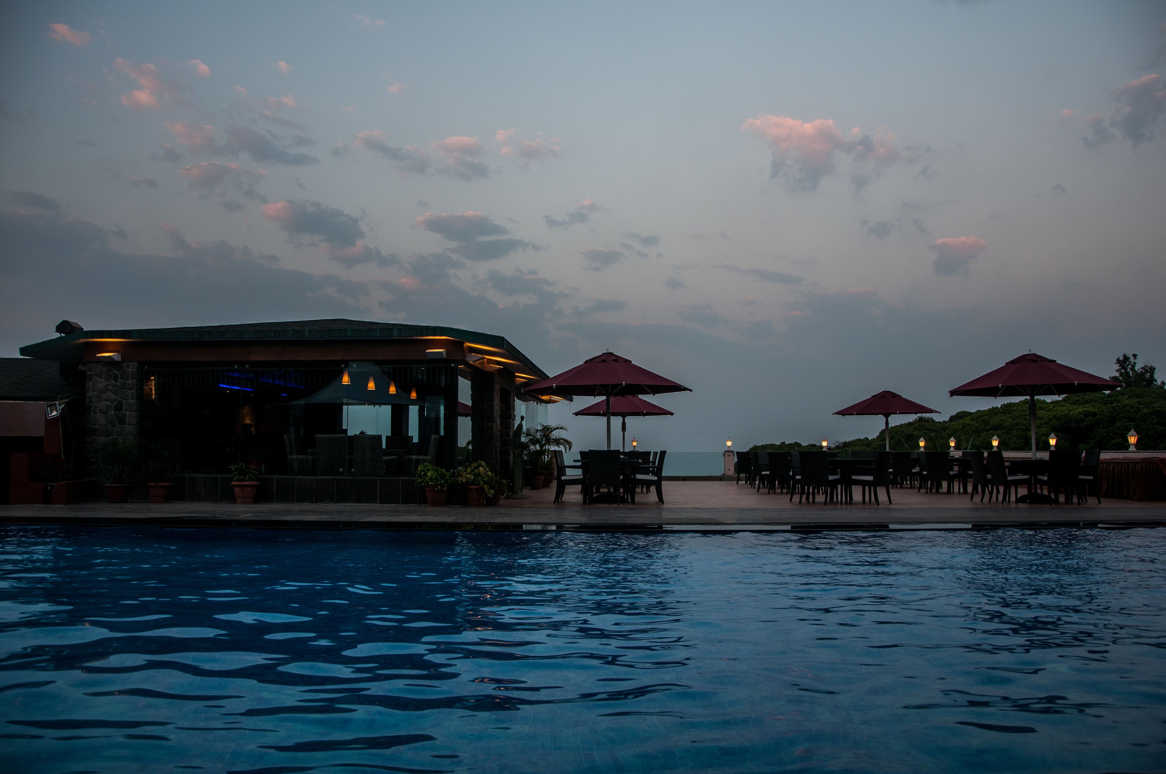 A poolside area with outdoor seating and umbrellas, overlooking a body of water.