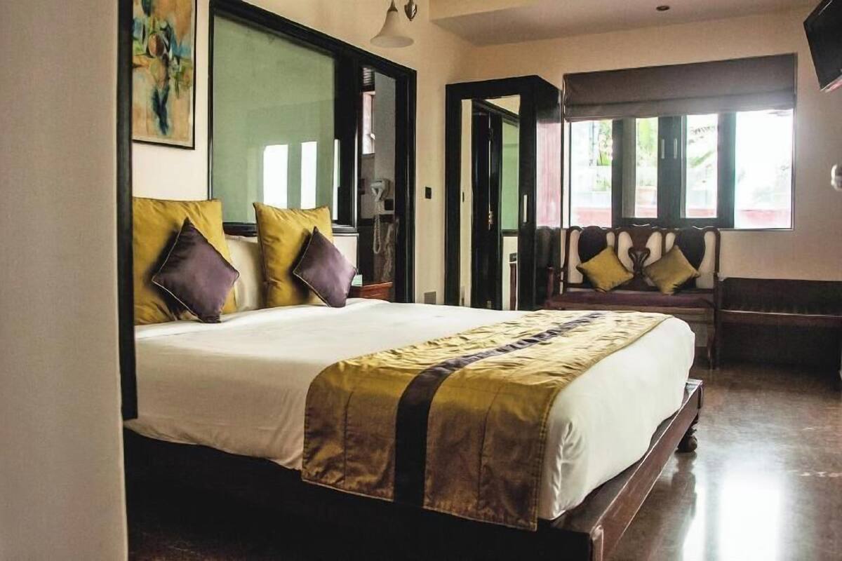 A hotel room with a large bed, a mirror, a window, and a door leading to another room.