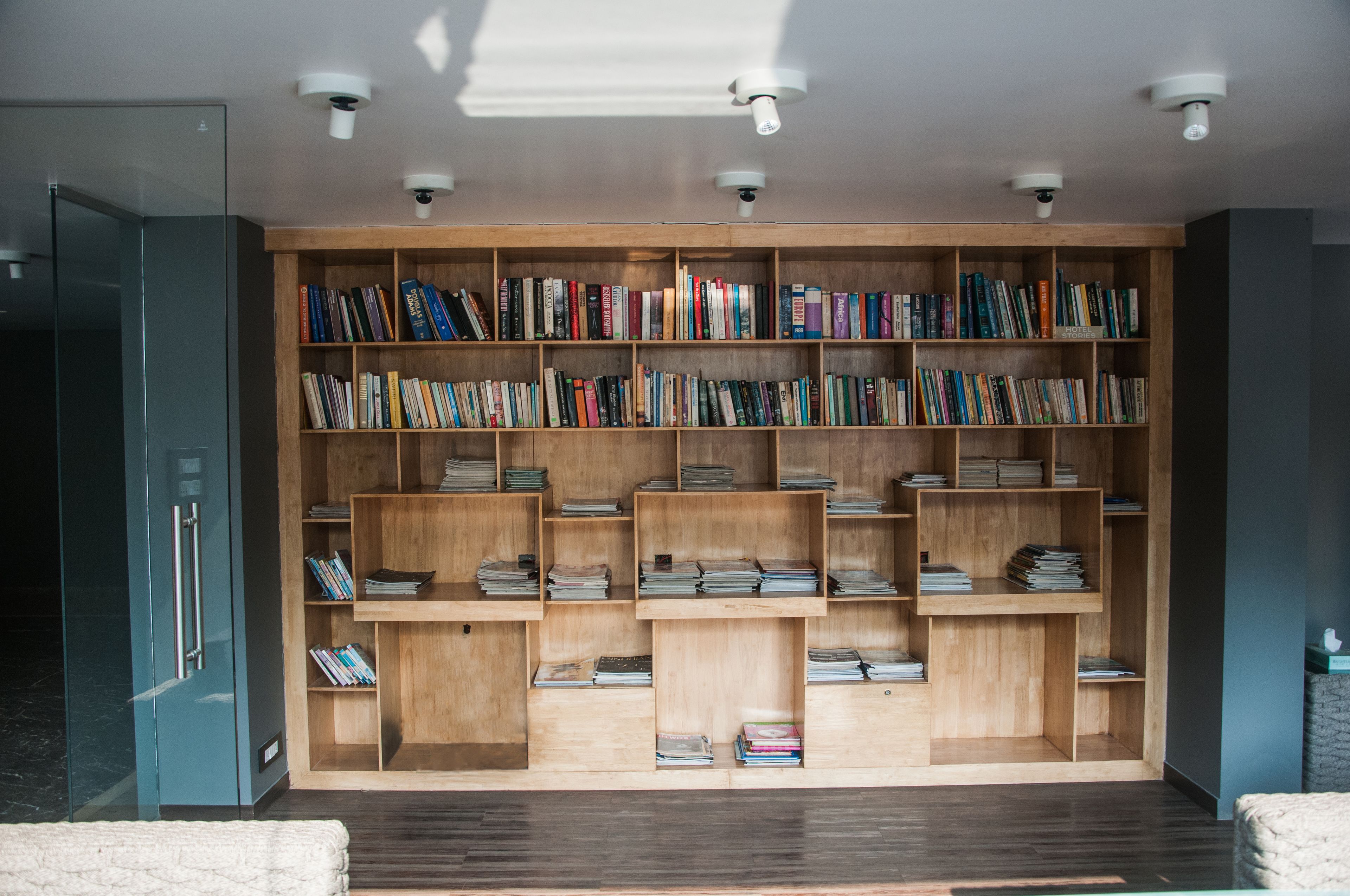 A modern library with wooden bookshelves filled with books, a glass door, and ceiling-mounted security cameras.