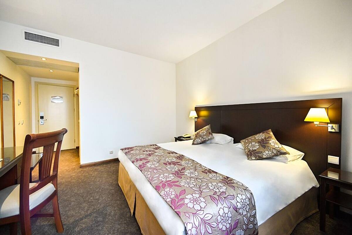 A hotel room with a bed, two bedside lamps, a wooden chair, and a desk.