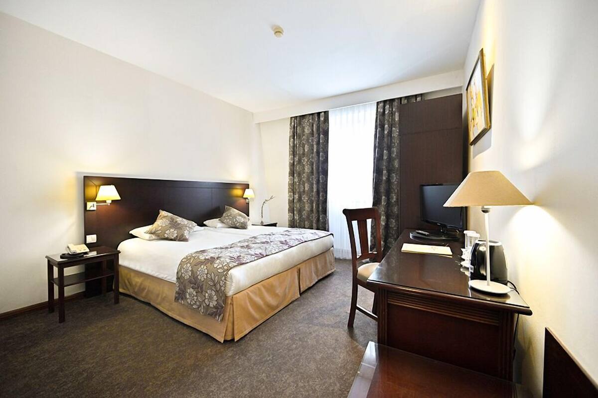 A hotel room with a bed, bedside tables, a desk, a chair, and a television.