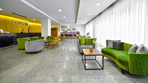 A modern lobby with green and grey sofas, yellow chairs, and a reception desk. - Europe Hotel (Yerevan)