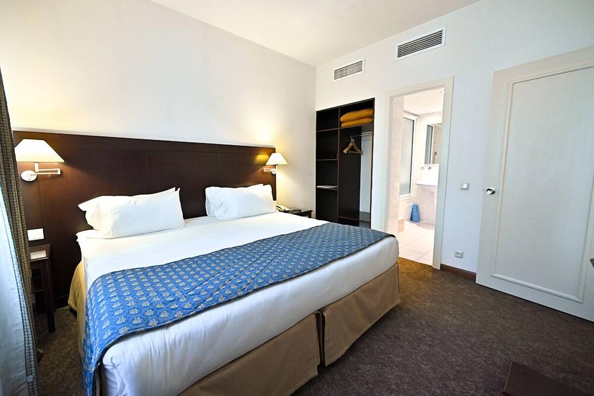 A hotel room with a large bed, a wardrobe, and a bathroom visible through an open door.
