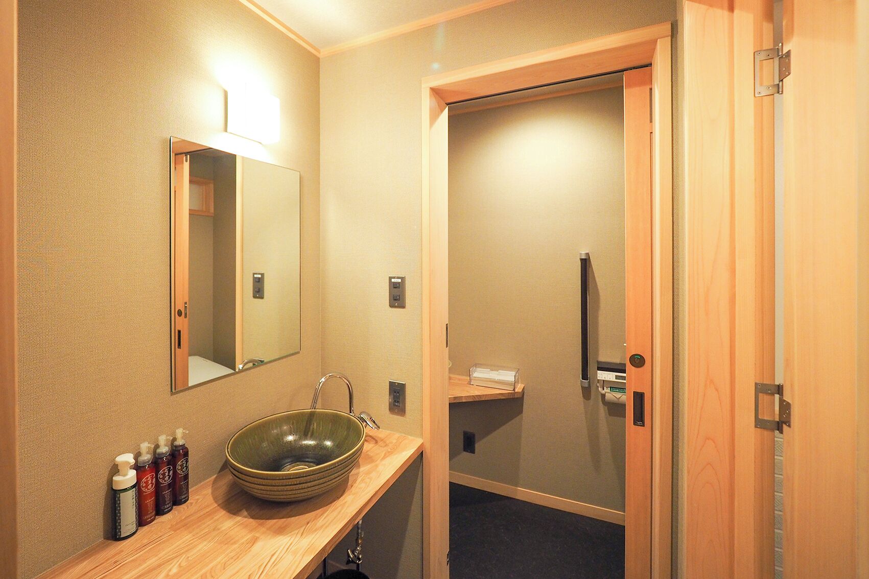 A bathroom with a wooden vanity, a large mirror, and a green bowl sink. There are toiletries on the counter and a towel rack above the sink.
