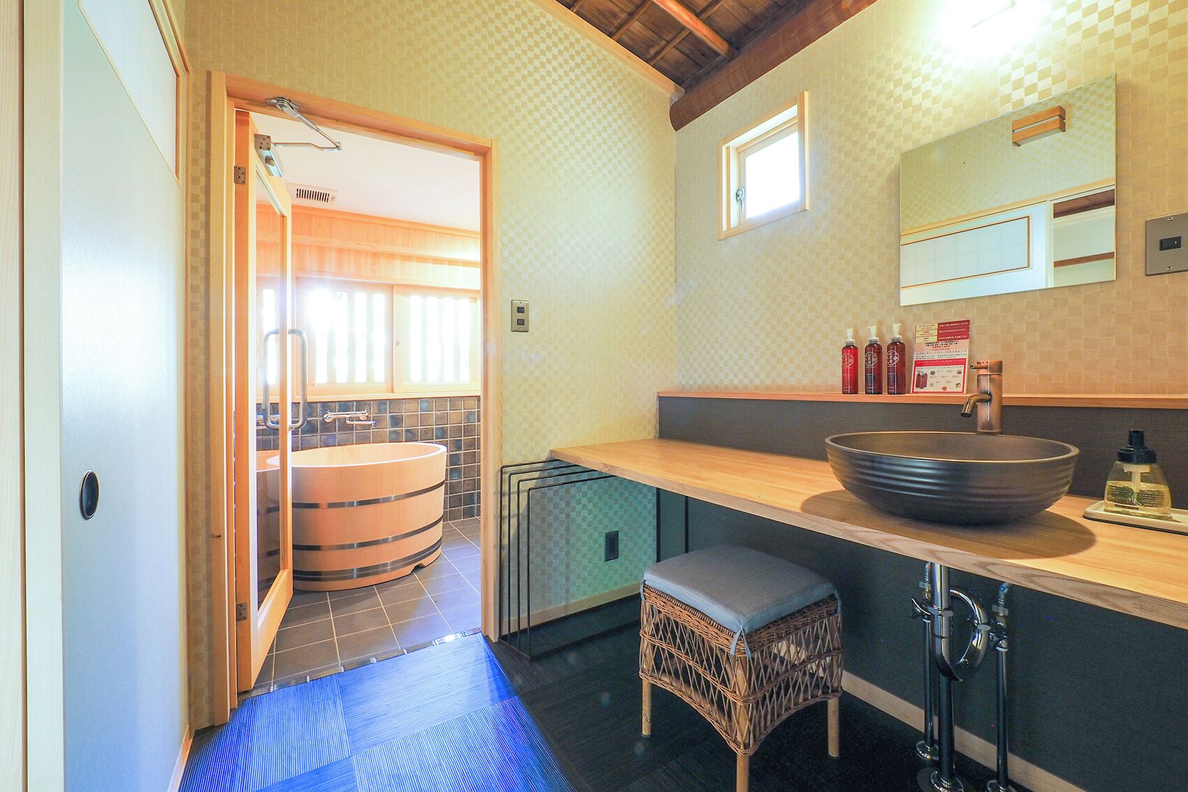 A bathroom with a large wooden bathtub, a sink with a large bowl, and a small stool.