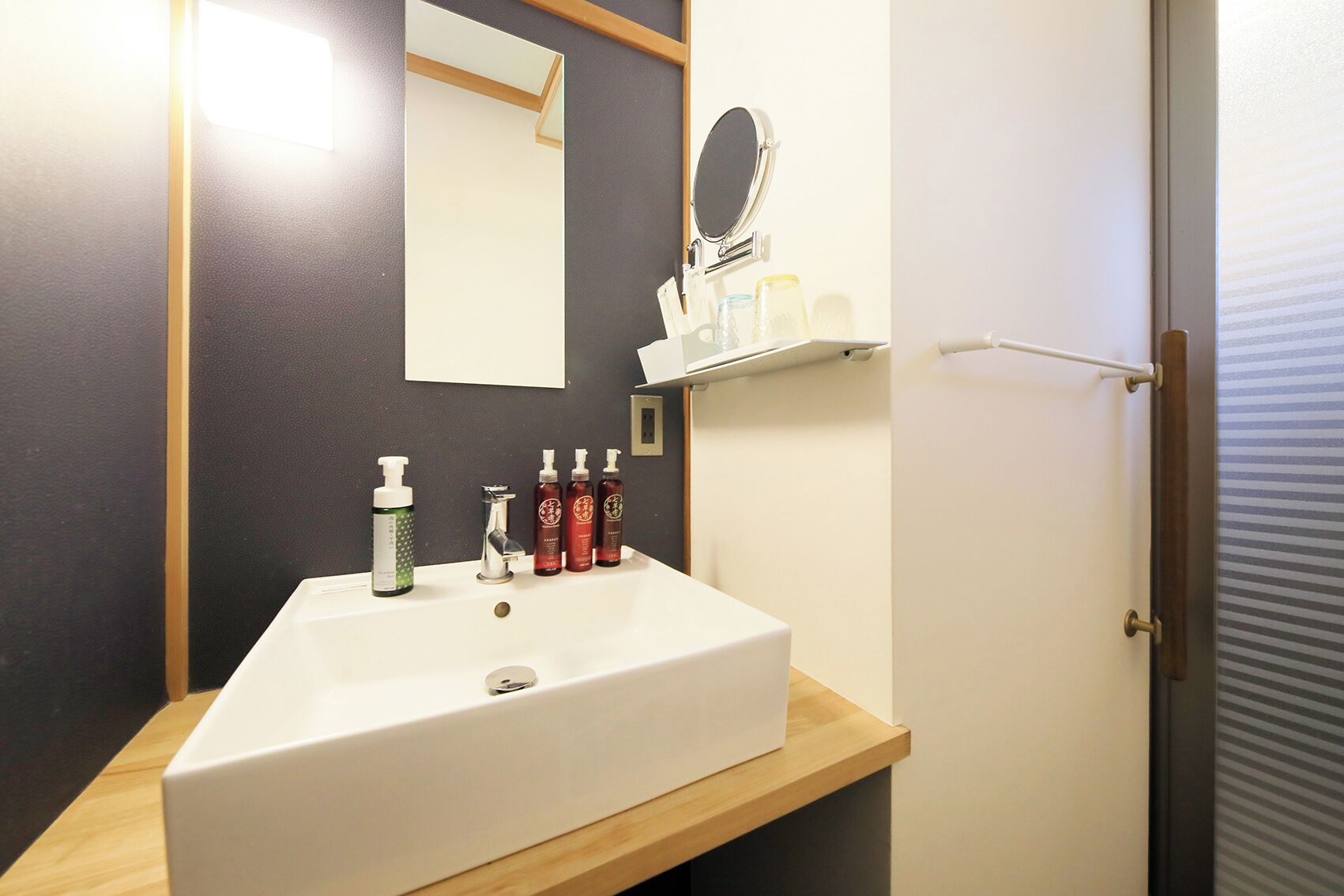 A bathroom with a white sink, a mirror, and a shelf with toiletries.