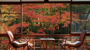 A room with two wicker chairs and a small table, large windows with a view of red autumn trees. - Arai Ryokan (Izu)
