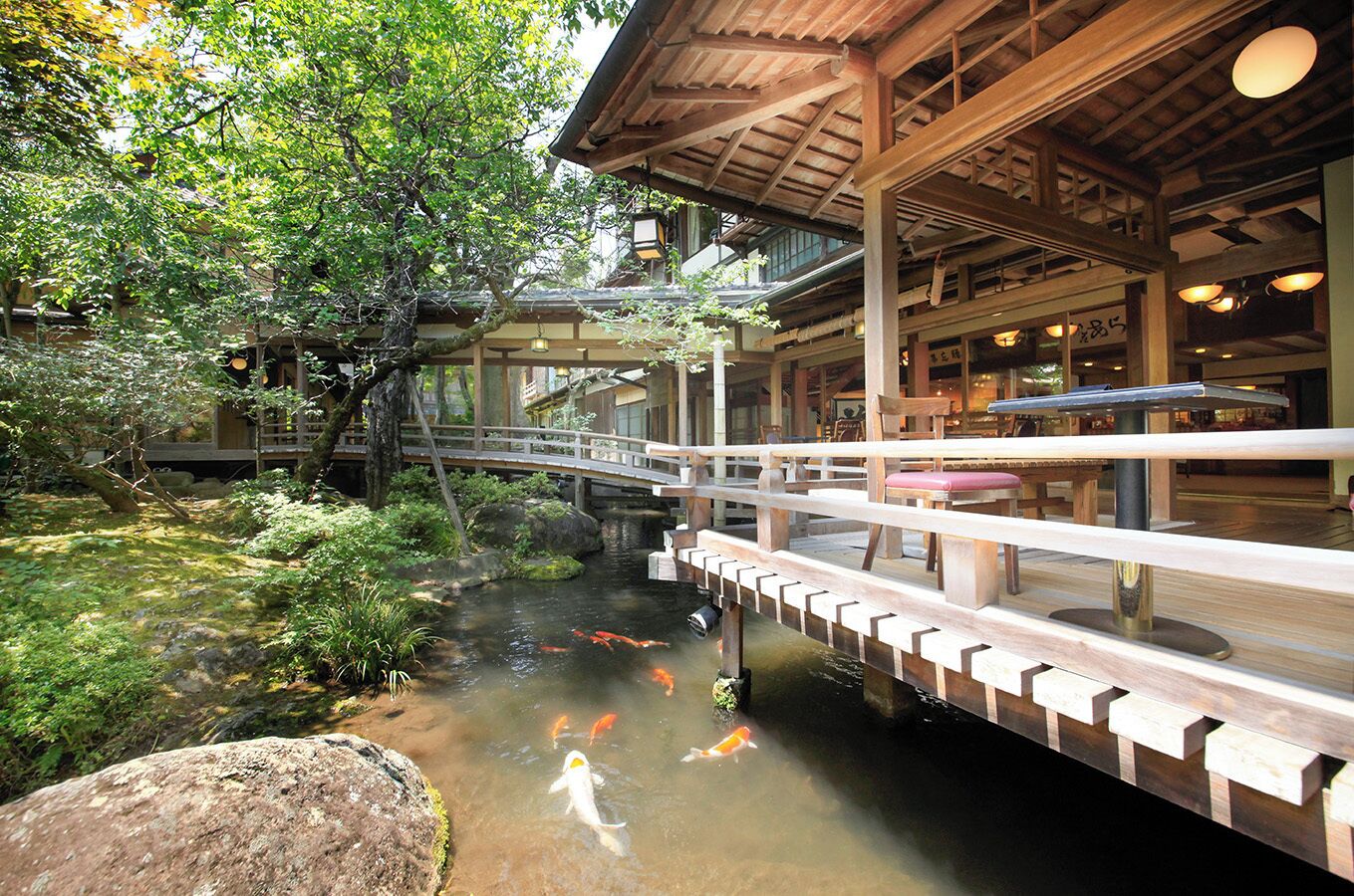 A traditional Japanese garden with a koi pond, wooden bridge, and a building with a wooden roof.