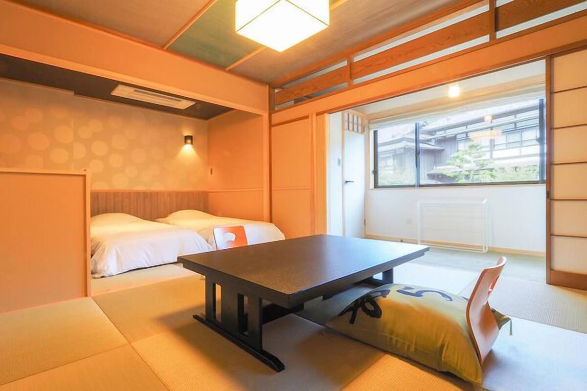 Ein traditioneller japanischer Raum mit Tatami-Boden, einem niedrigen Tisch und einem Bett mit weißer Bettwäsche.